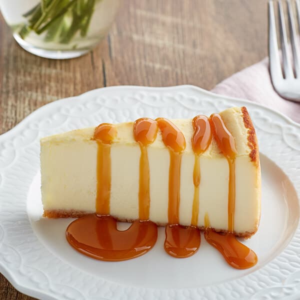 A slice of cheesecake drizzled with caramel sauce on a white plate.