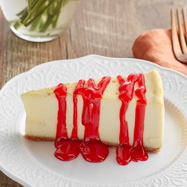 A slice of cheesecake topped with bright red strawberry flavoring sauce on a white plate.